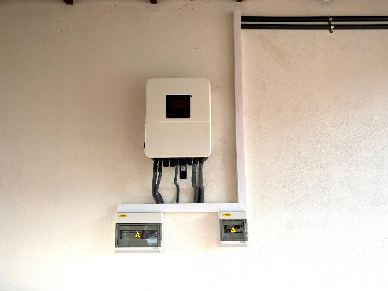 Deye hybrid inverter installed on a wall above two protection enclosures